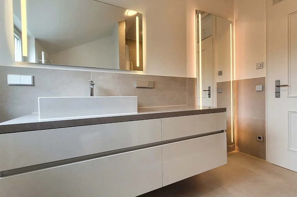 Badsanierung Kosten Mannheim – neu renoviertes Badezimmer mit großzügigem Waschtisch, Aufsatzwaschbecken, modernen Armaturen, großformatigen Fliesen und beleuchteten Spiegeln