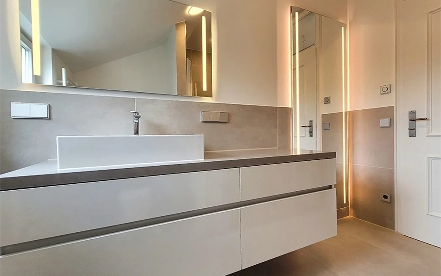 Badsanierung Kosten – ein moderner Badezimmerbereich nach Badrenovierung durch ALLSAN zeigt ein ruhiges, stilvolles Gesamt-Erscheinungsbild, die Bad-Beleuchtung ist ein zentrales Designelement: Es gibt vertikale, indirekte LED-Lichtleisten, die dezent hinter dem Badezimmer Spiegel und einem weiteren Spiegelelement verlaufen
