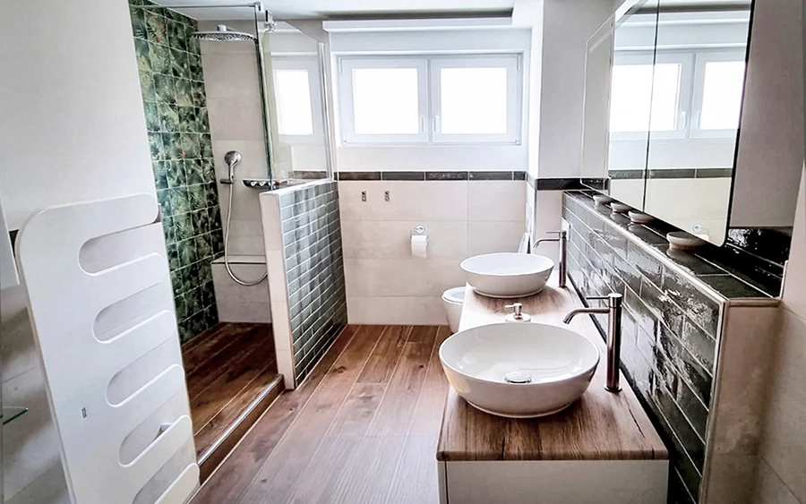 Fliesenleger Bad nach Renovierung mit offener, begehbarer Dusche und Eyecatcher Fliesen an der Rückwand mit Naturmotiv, Bodenfliesen in Holzoptik sowie hochglänzenden Metrofliesen im clean gestalteten Sanitärbereich mit edlen Waschschüsseln auf einem großzügigen Waschtisch für 2 Personen