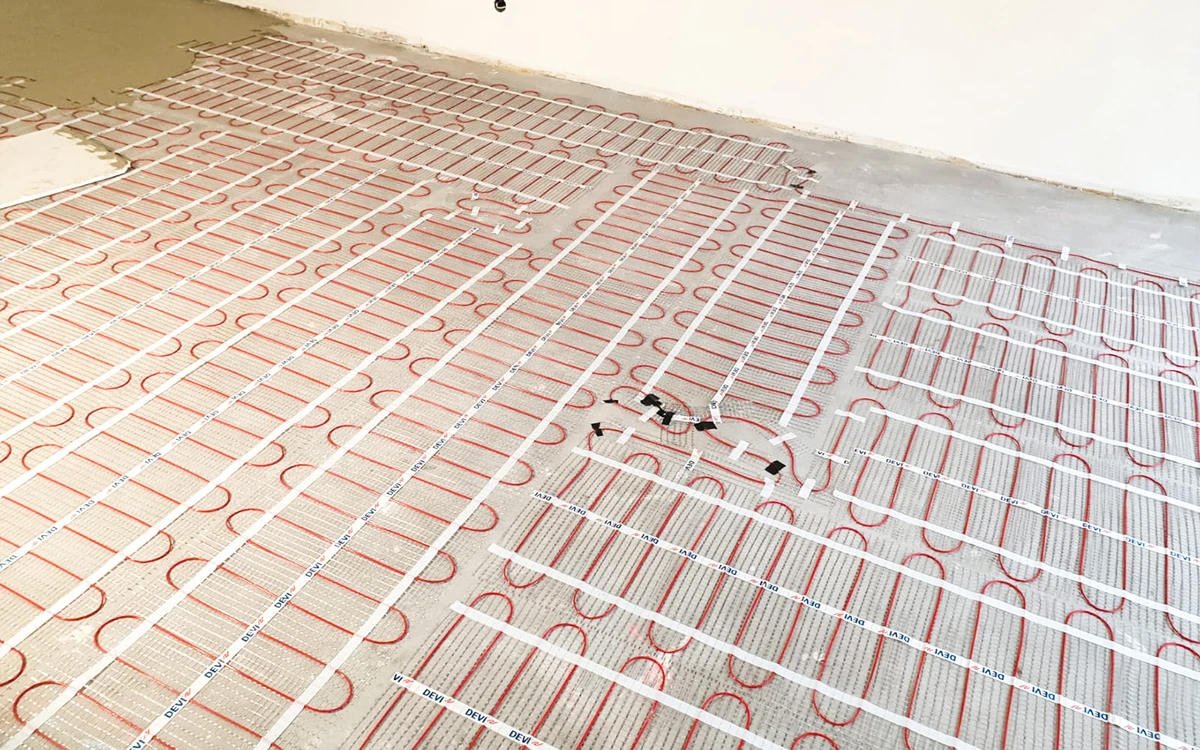 Verlegung Fußbodenheizung im Rohbau, rote Heizrohre sind gleichmäßig in Schleifen auf dem Boden befestigt, bereit für die Estrichverlegung