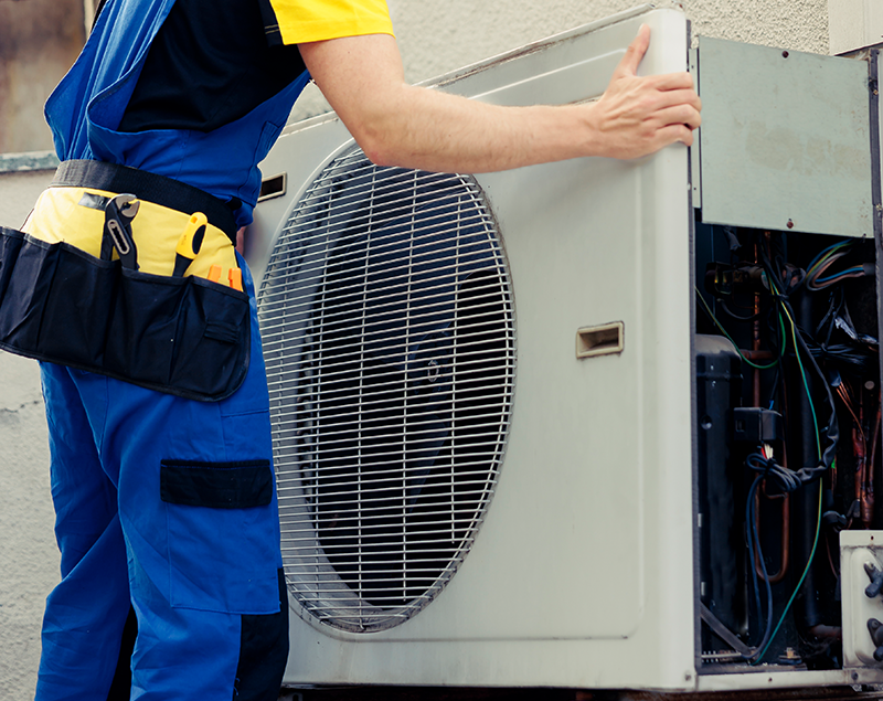 Wärmepumpen Installation - SHK Installateur - bei der Anbringung und Einrichtung einer Wärmepumpe Außeneinheit. Die Verkleidung des Geräts ist geöffnet, sodass Kabel und Technik sichtbar sind. Der Techniker trägt Arbeitskleidung und steht neben dem Gerät