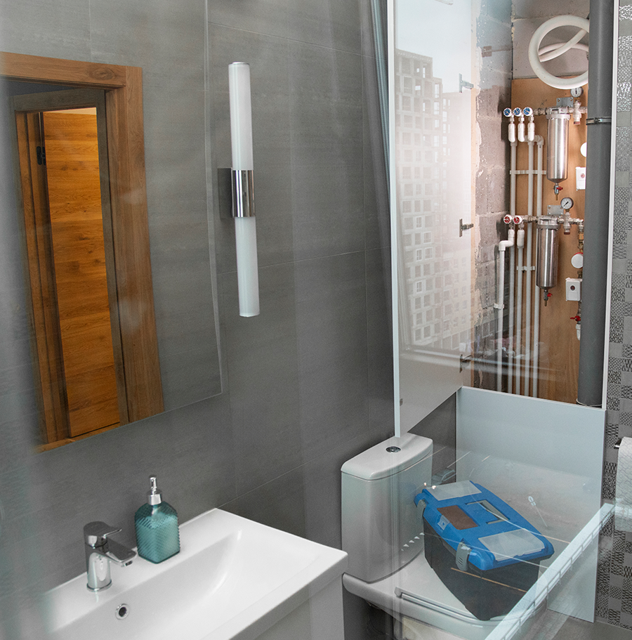 Sanitärfirma Heidelberg – ein Badezimmer während der Installationsphase. Im Vordergrund ist ein weißer Waschtisch zu sehen dahinter Sanitär- und Heizungsrohre und ein Werkzeugkasten für die laufenden Montagearbeiten freiliegende Wasserleitungen, Absperrventile und Filterelemente zu sehen, die sauber und übersichtlich an der Wand montiert sind. Die Wand ist teilweise unverkleidet, was den technischen Aufbau der Sanitärinstallation sichtbar macht. Insgesamt vermittelt das Bild einen Eindruck von präziser, strukturierter Handwerksarbeit im Zuge einer Badsanierung oder Modernisierung.